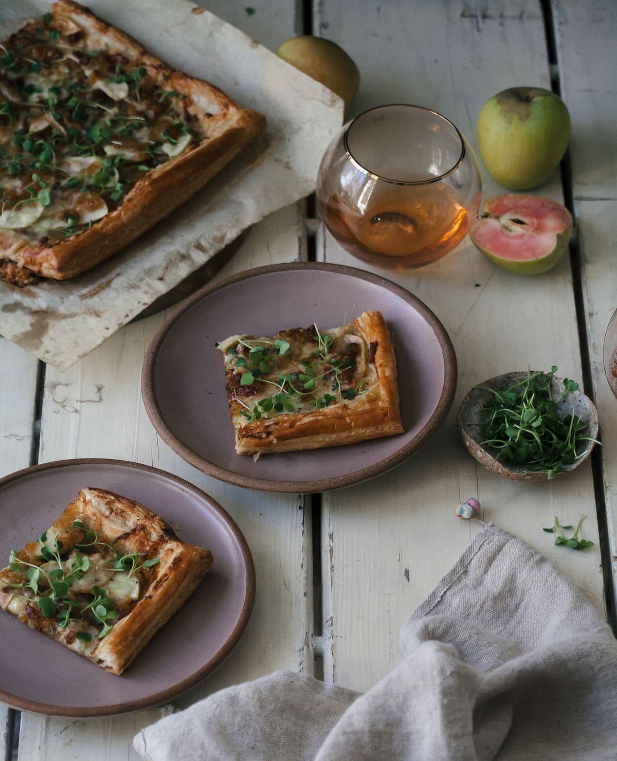 A rustic apple and gruyere tart on a wooden board, garnished with fresh thyme
