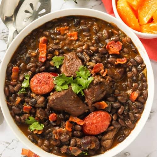 close-up of various cuts of smoked meat being added to a pot of feijoada