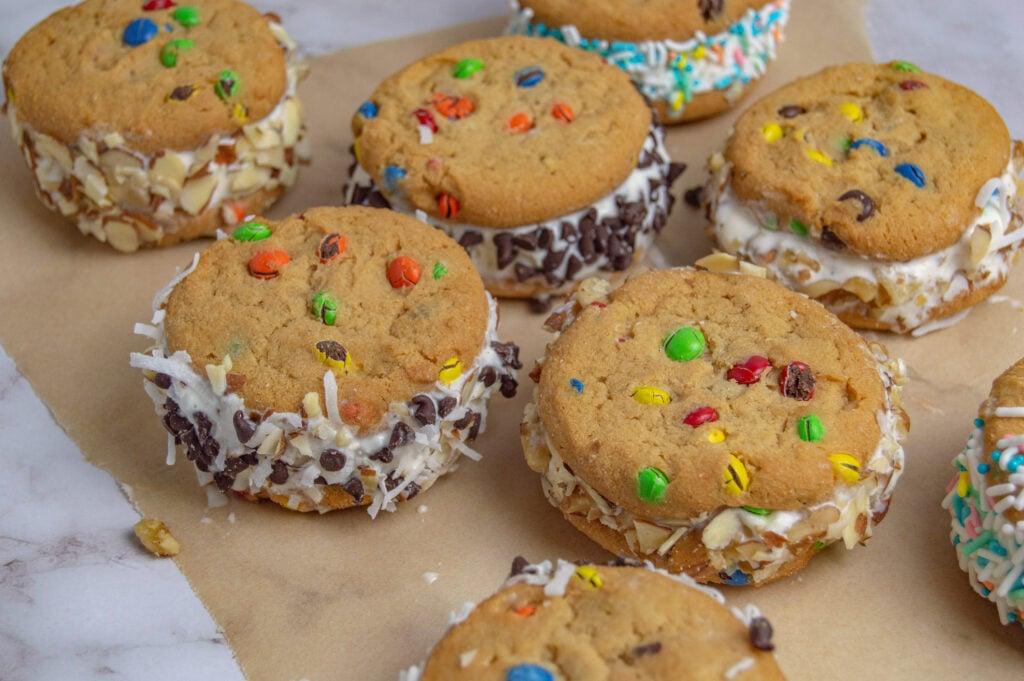 Various types of cookies and ice cream flavors displayed together alongside various toppings like sprinkles, chocolate syrup, fruit, etc.