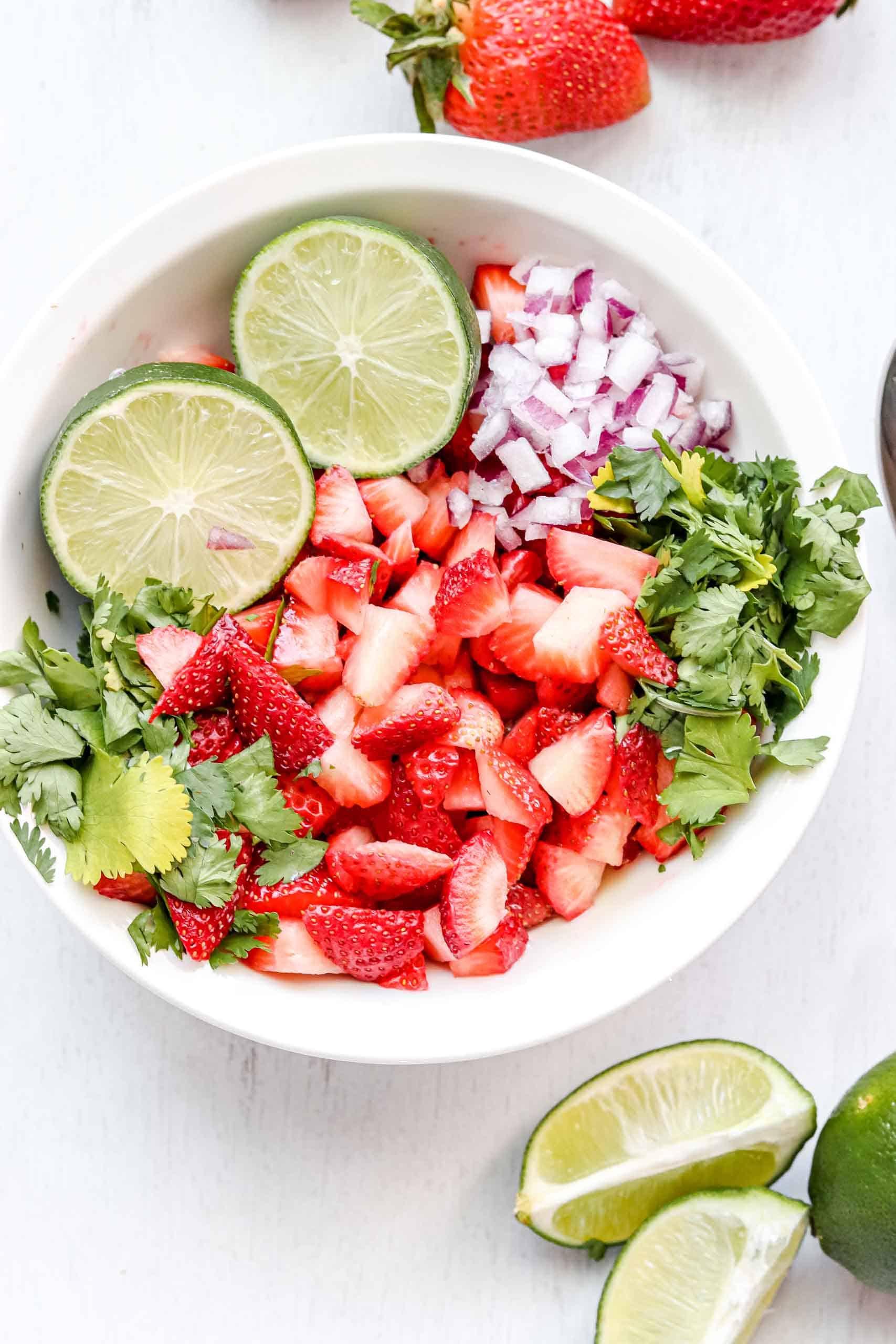 A vibrant bowl of strawberry salsa with fresh basil leaves, garnished with a lime wedge.