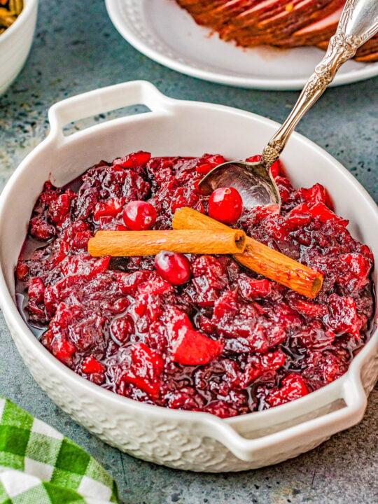Vibrant homemade cranberry apple sauce in a rustic bowl with cinnamon sticks and fresh cranberries, cozy holiday background