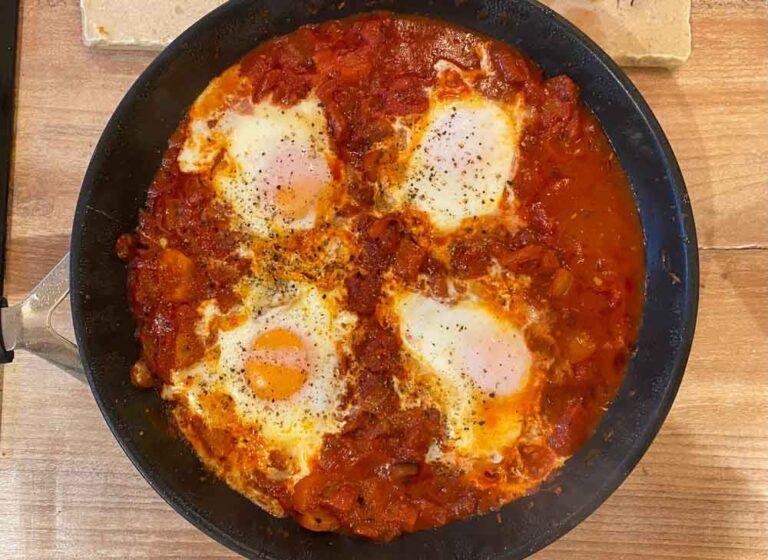 Close-up shot of a fork piercing a runny egg yolk in the shakshuka, revealing the creamy texture
