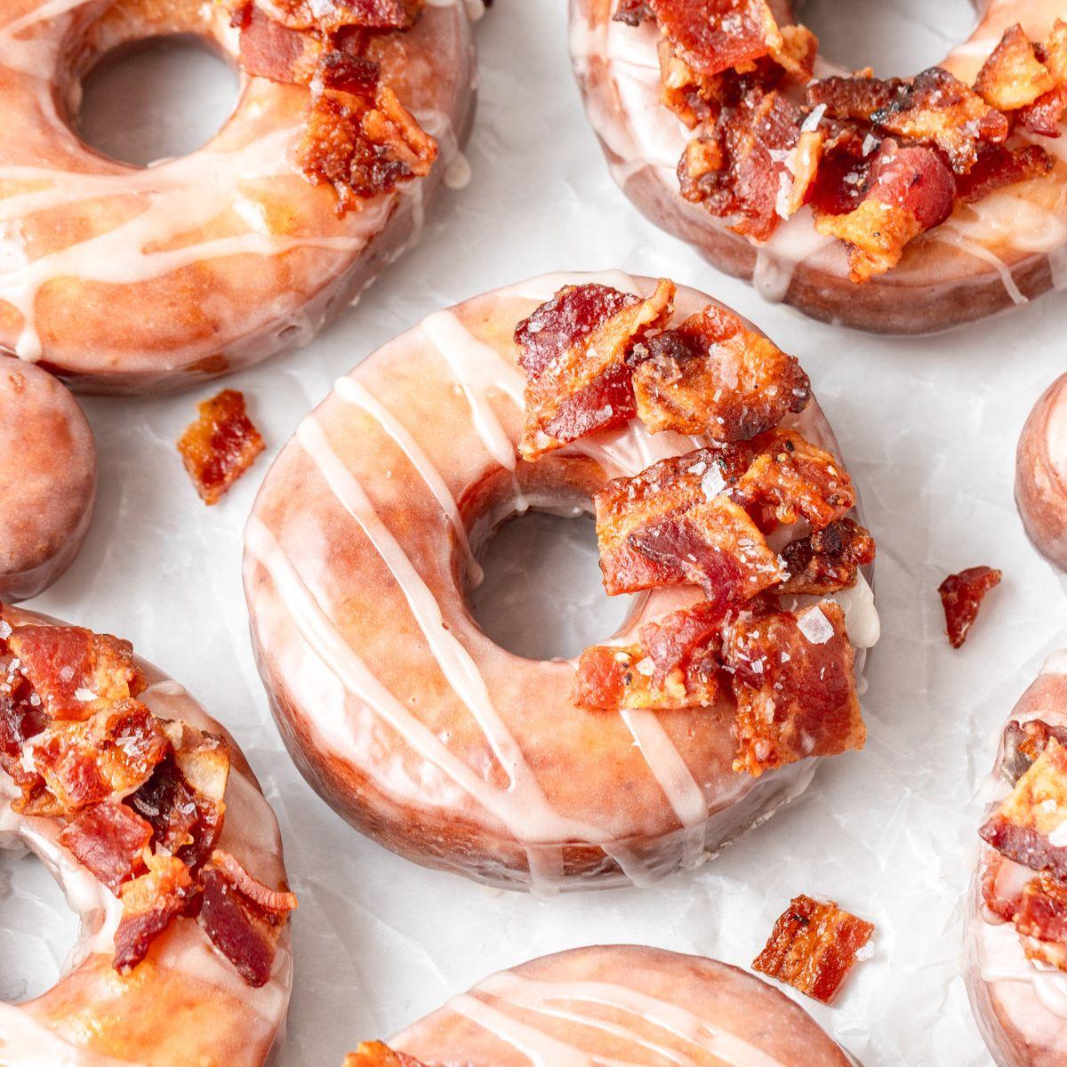 Close-up shot of golden-brown maple bacon donuts with a drizzled glaze, glistening from the light