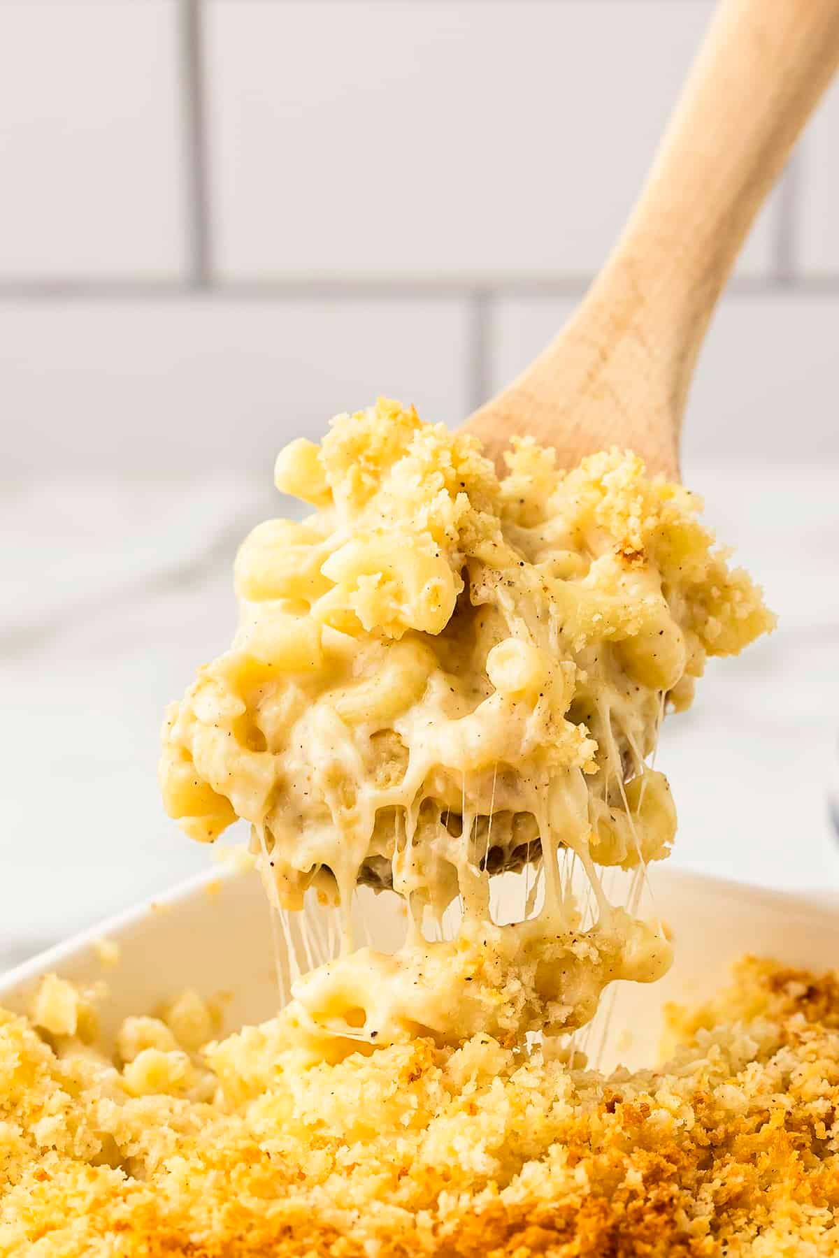 Close-up of a spoon scooping into baked mac and cheese, showing the gooey cheese pull and crispy topping.