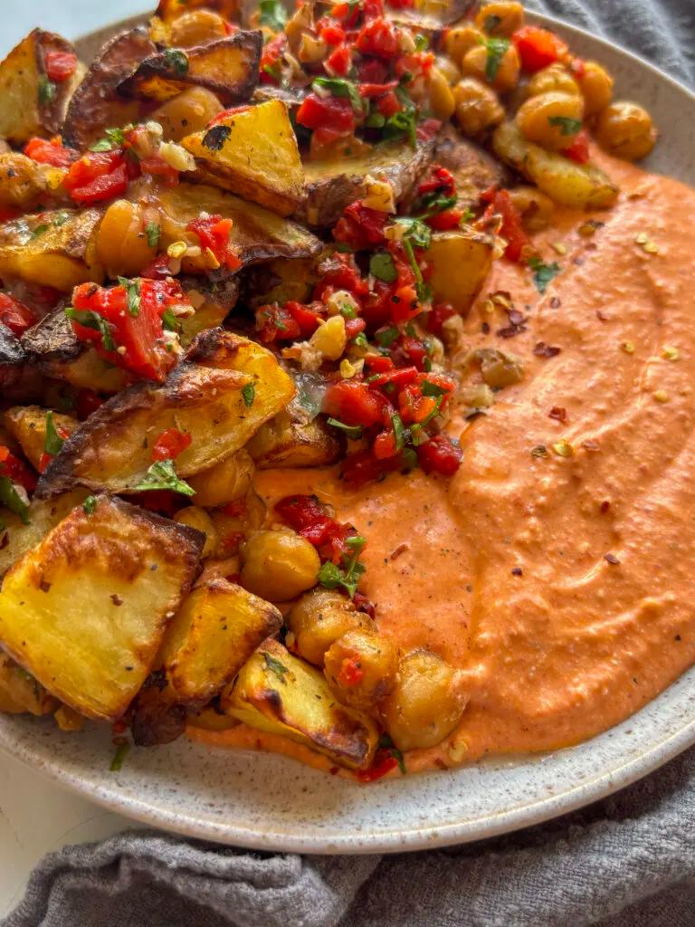 Close-up shot of boiled potatoes with roasted red peppers and feta, garnished with fresh herbs