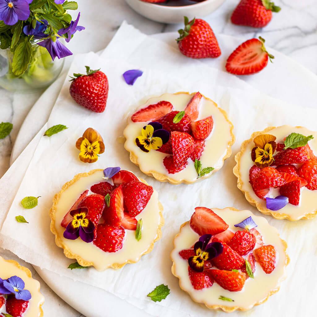 Close-up of fruit tarts with white chocolate ganache and fresh strawberries, garnished with mint