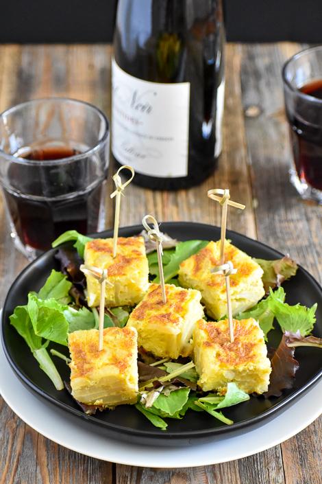 A platter of sliced Tortilla Española, garnished with fresh parsley, alongside a glass of Spanish wine