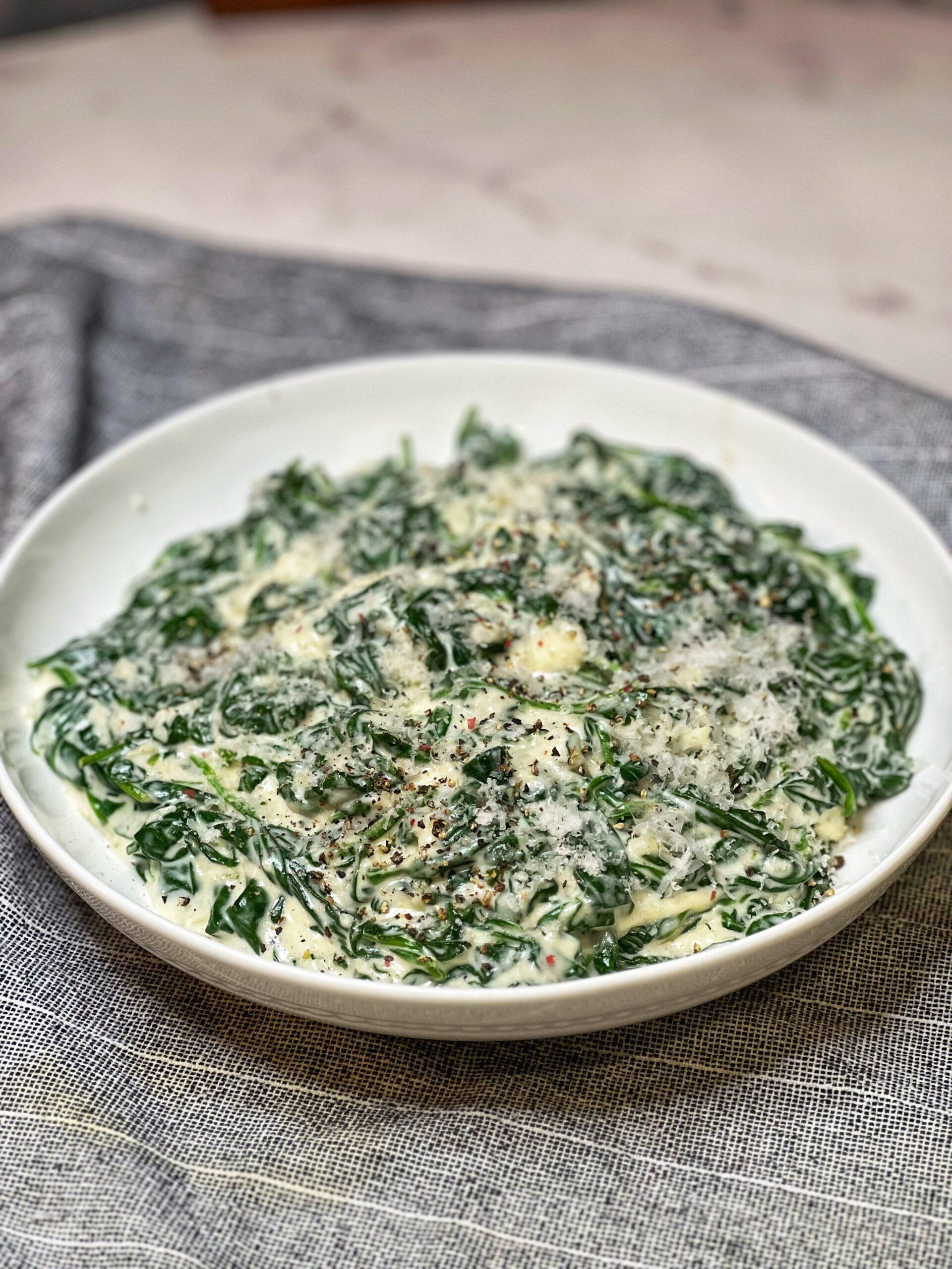 Gourmet creamed spinach in a white bowl, garnished with fresh herbs