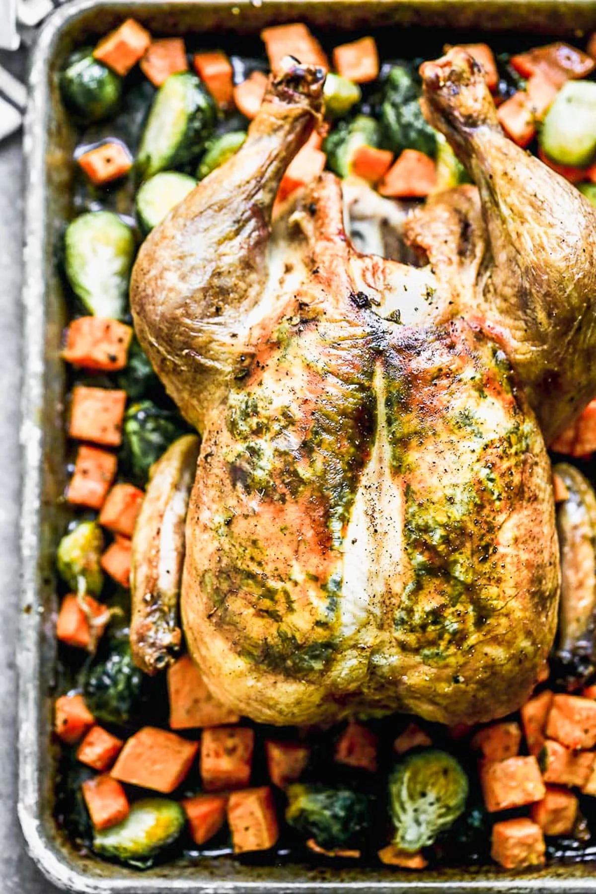 A golden-brown roasted chicken with a vibrant green sage sauce drizzled over it.