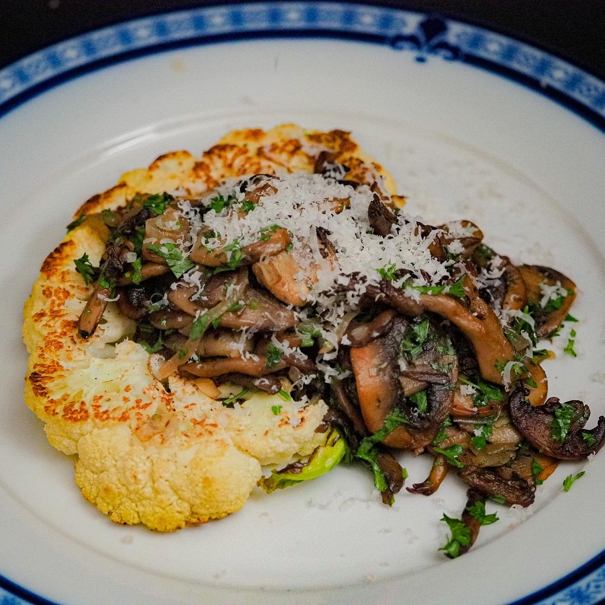 Close-up of perfectly seared cauliflower steaks topped with balsamic glaze and sauteed mushrooms, garnished with fresh herbs