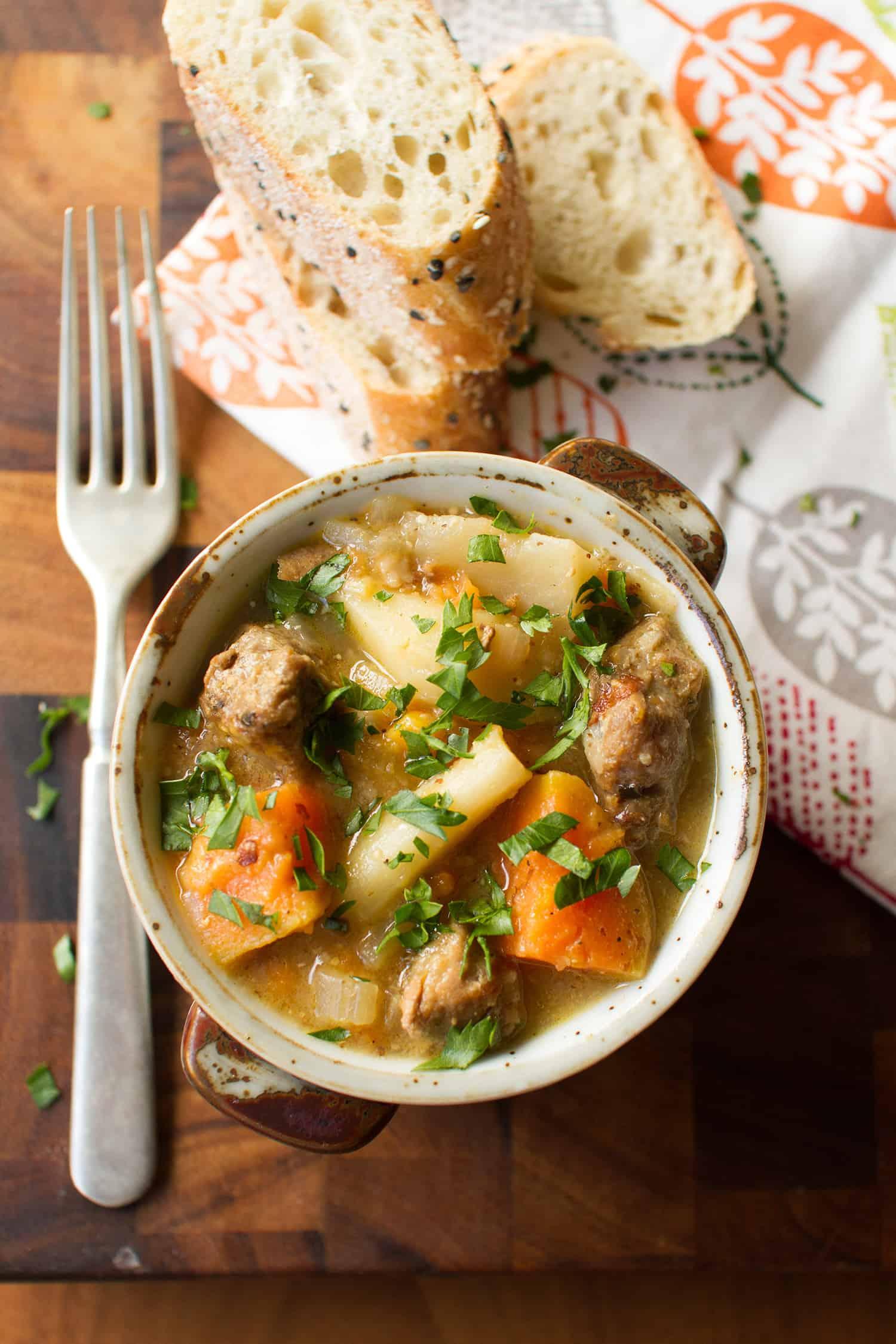Close-up shot of a steaming bowl of pork stew with apples and cider, garnished with fresh parsley
