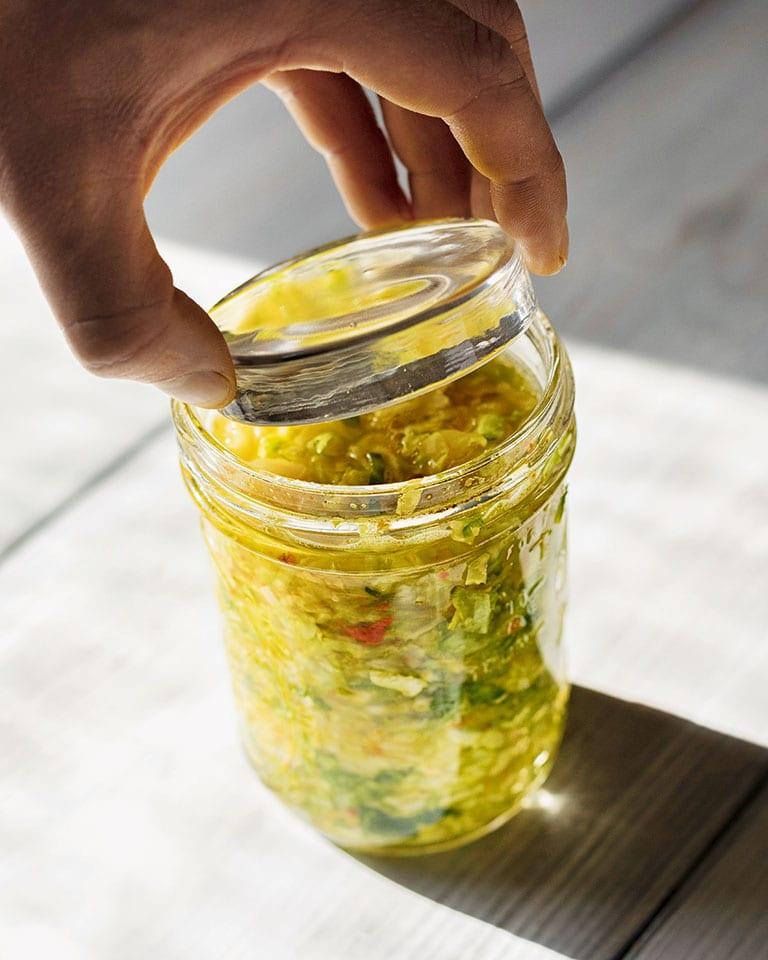A jar of golden olive oil infused with vibrant sauerkraut, garnished with fresh dill