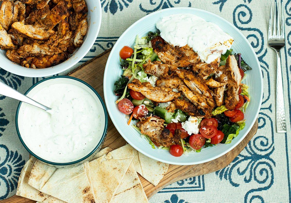 A table setting with a bowl of gyro-flavored salsa and various other Greek-inspired dishes