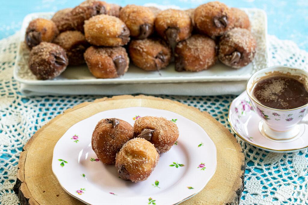 A table set with a plate of Nutella-stuffed churros donuts and mugs of coffee