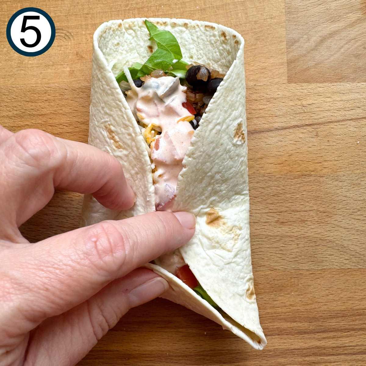 a person assembling a black bean corn jicama wrap, close-up of hands carefully rolling the tortilla