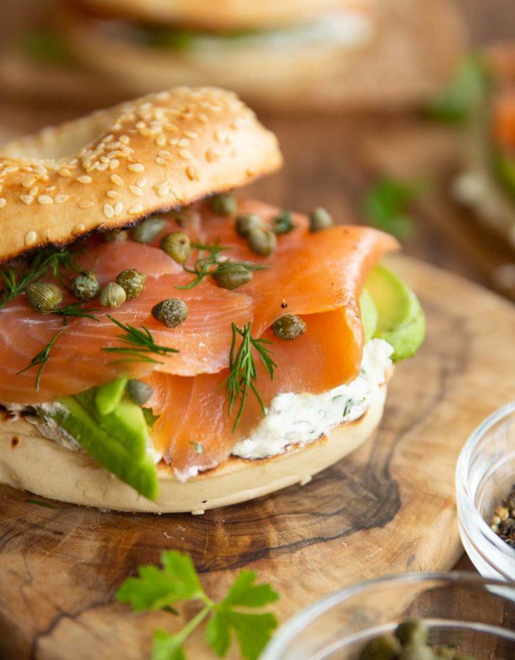 Close-up shot of a poppy seed bagel with smoked salmon, cream cheese, and capers on a rustic wooden board