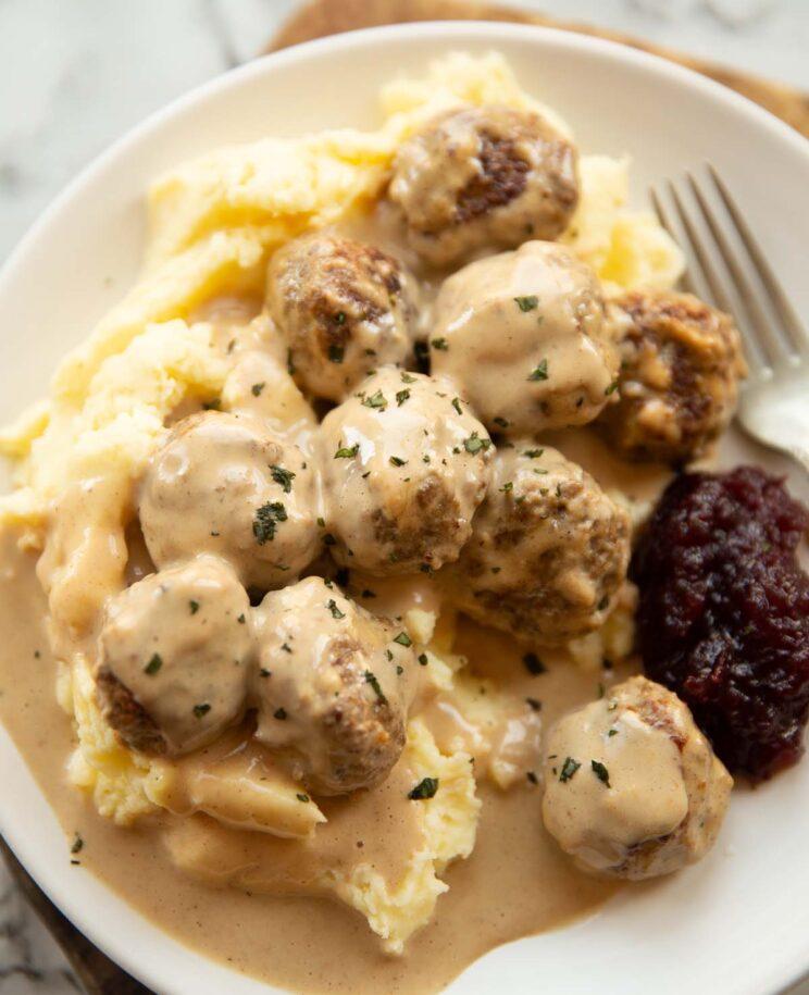 Close-up shot of Köttbullar with creamy mustard gravy, served with mashed potatoes and lingonberry jam.