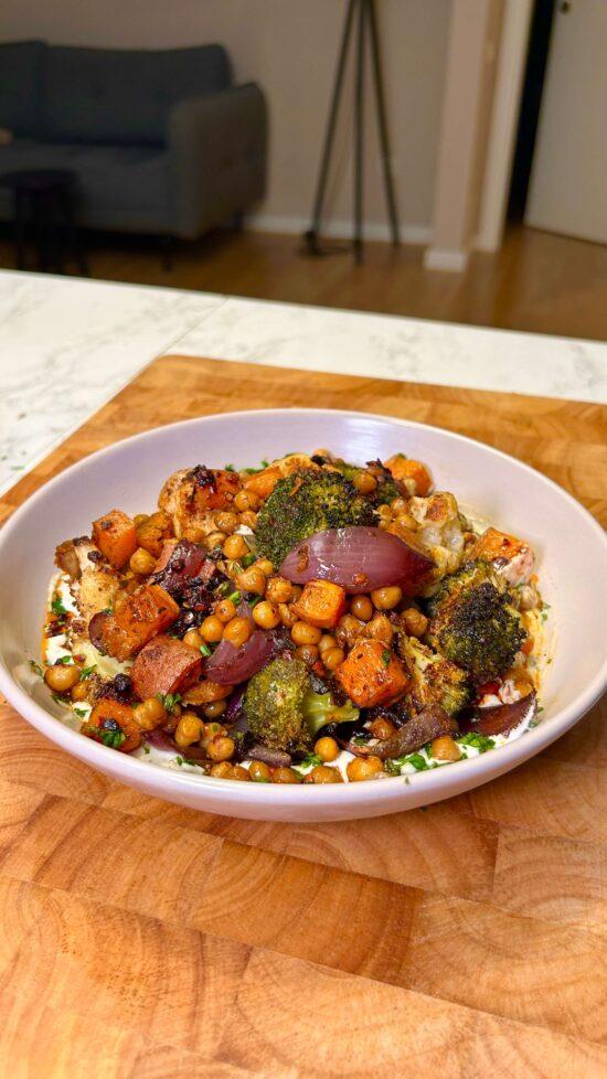 A platter of colorful roasted vegetables arranged artfully next to a stack of warm rotis and a small bowl of tahini dressing