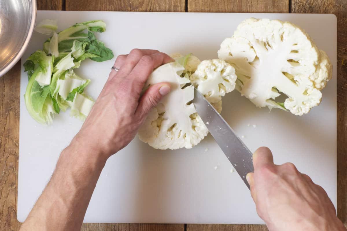 Overhead shot of raw cauliflower head being sliced into steaks on a cutting board