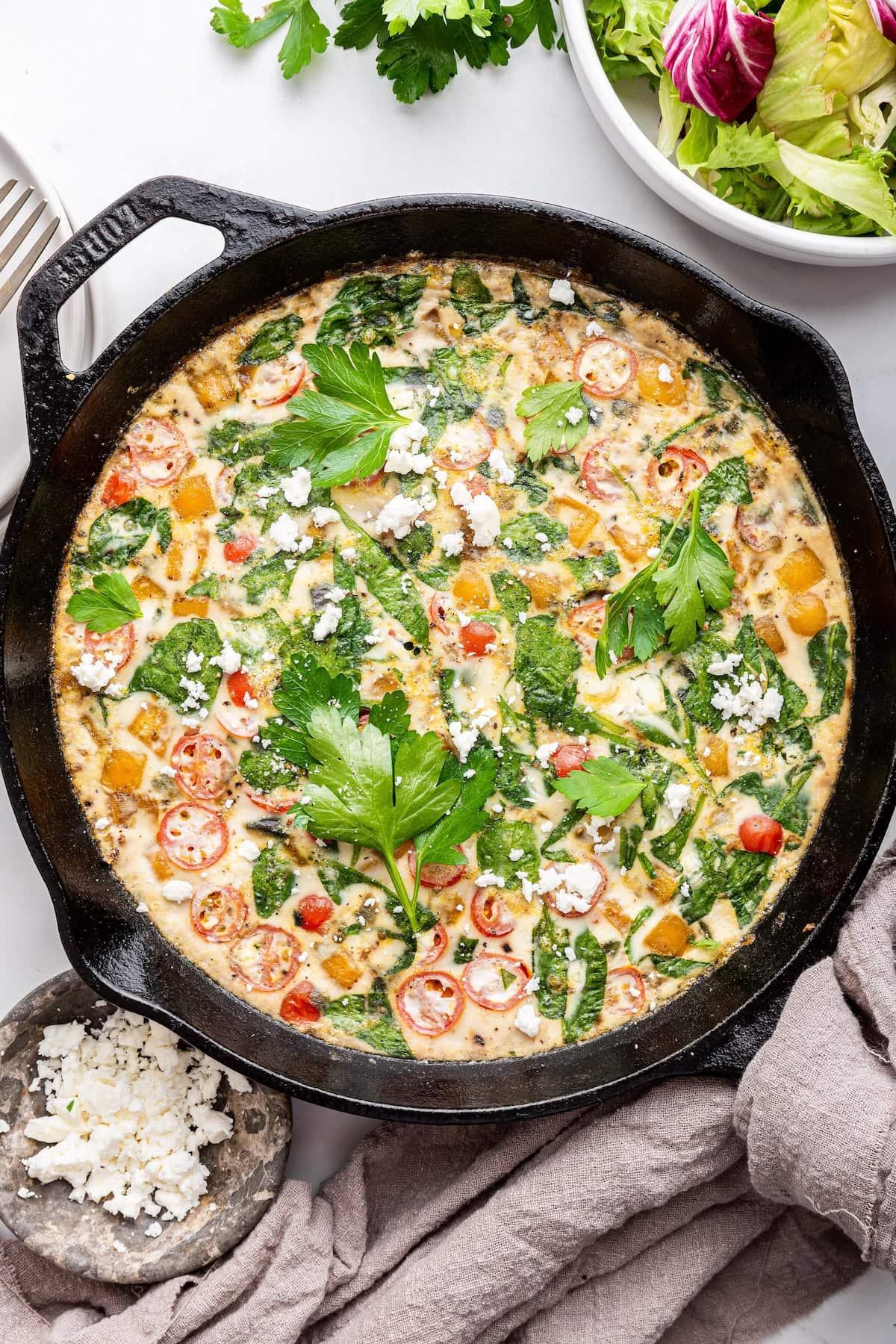 A whole Squash and Spinach Frittata with Feta in a cast iron skillet, garnished with fresh herbs
