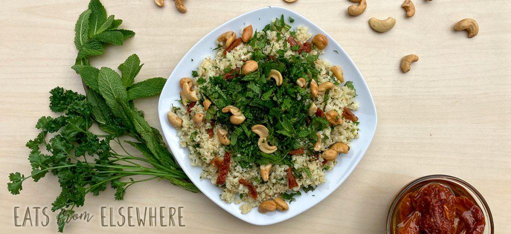 A vibrant and colorful bowl of cauliflower rice with sun-dried tomatoes, garnished with fresh herbs
