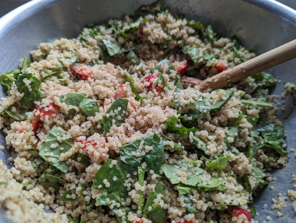 close-up of poppy seed dressing being drizzled on strawberry spinach quinoa salad