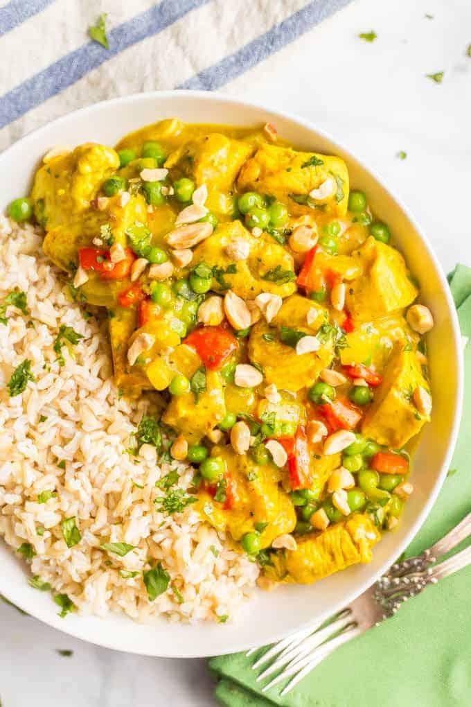 Close-up shot of a bowl of yellow curry rice with chicken, peas, and cilantro