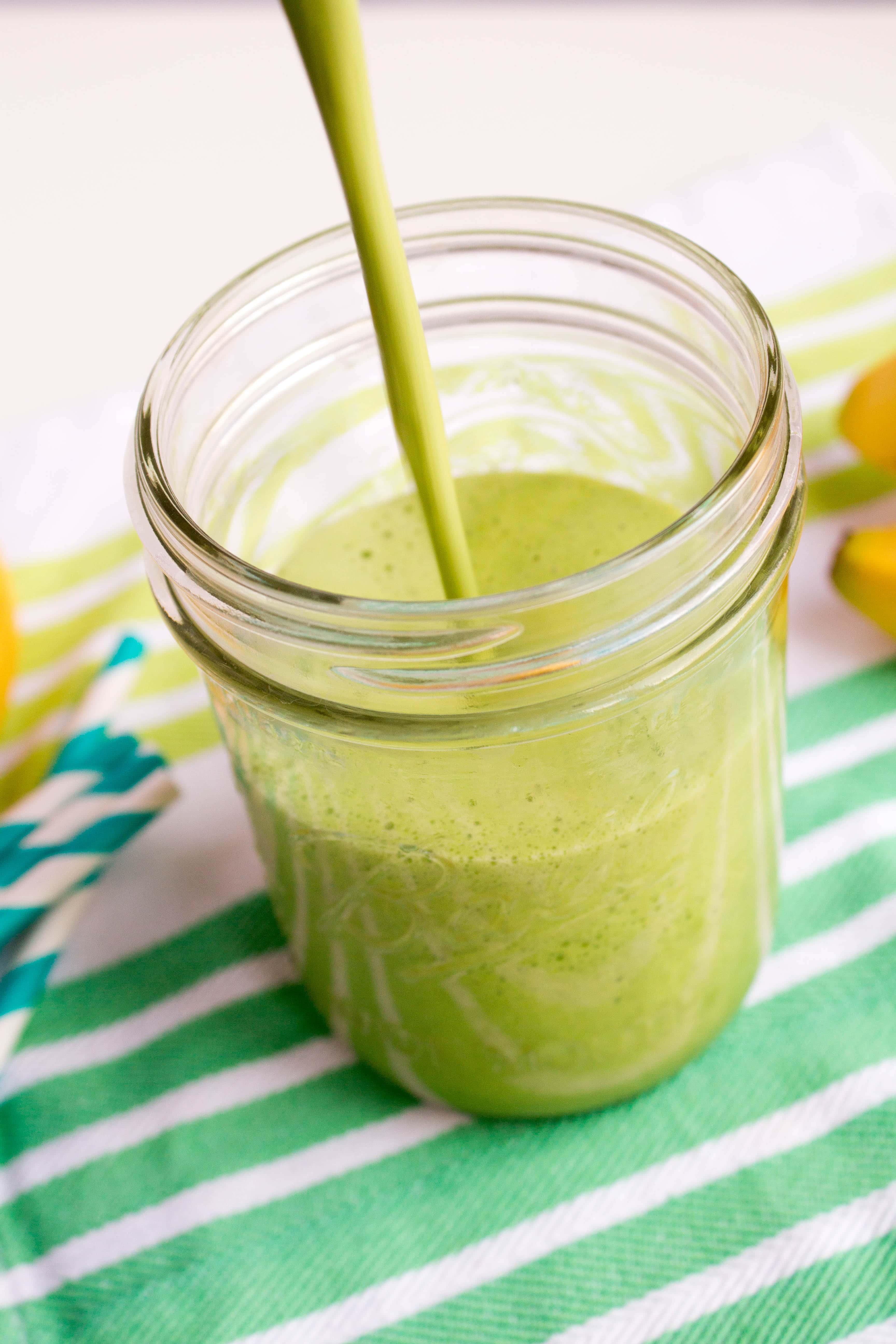 Close-up shot of a vibrant green smoothie in a glass with fresh ingredients like banana and spinach arranged around it.