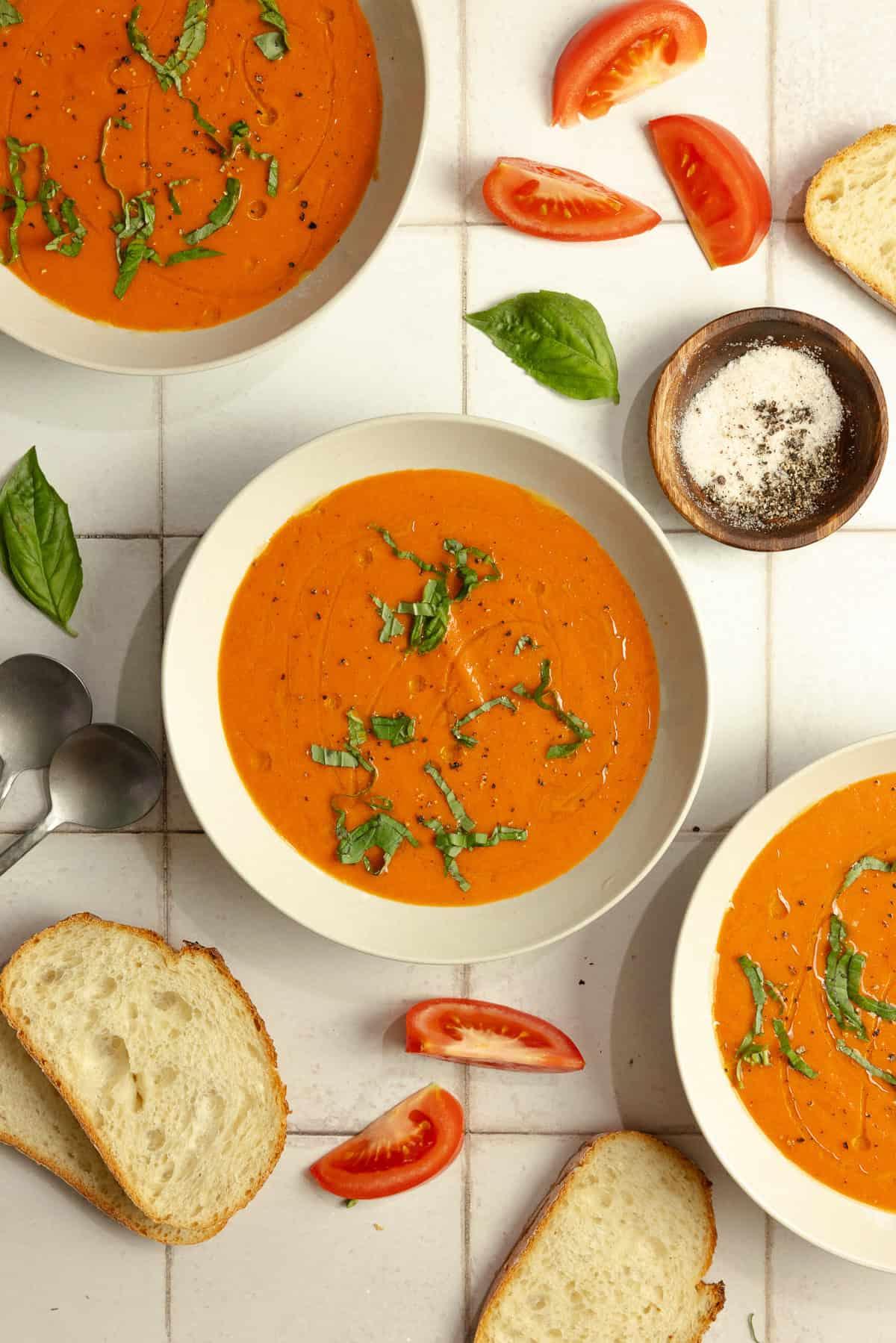 rustic table setting with bowls of roasted red pepper tomato soup, crusty bread, and fresh basil