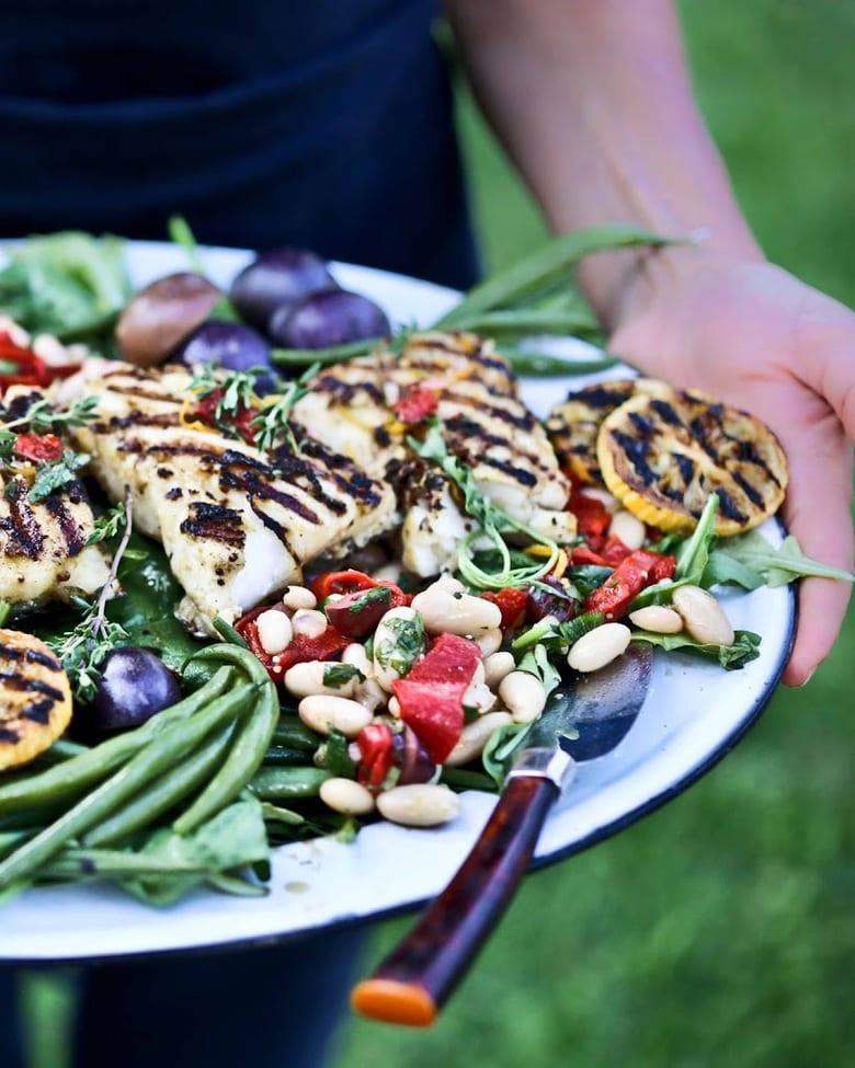 Person serving grilled fish fillets with a side salad