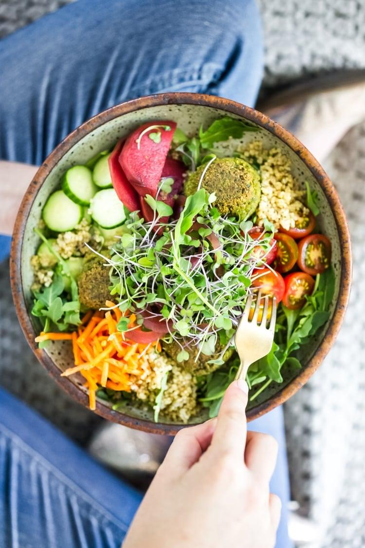 Close up of a person adding fresh herbs to a falafel bowl