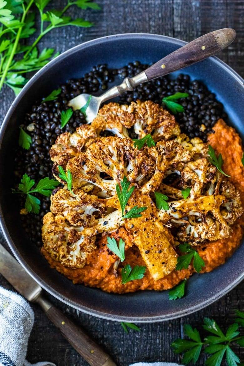 A serving of roasted potatoes and cauliflower with romesco sauce, garnished with fresh herbs.