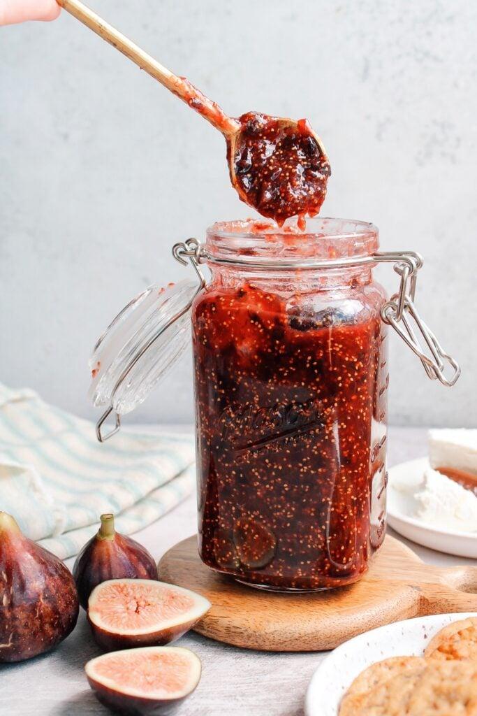 Jar of homemade lingonberry fig jam with fresh lingonberries and figs in the background