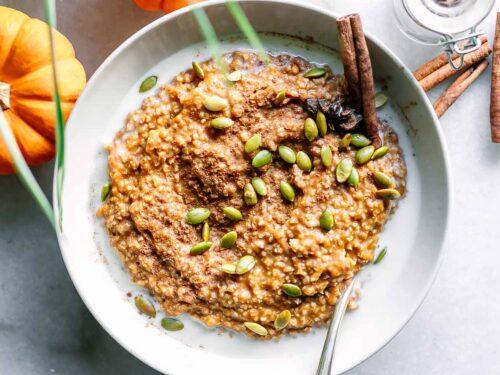 A rustic bowl of pumpkin spice oatmeal with various toppings, garnished with cinnamon and a sprig of rosemary