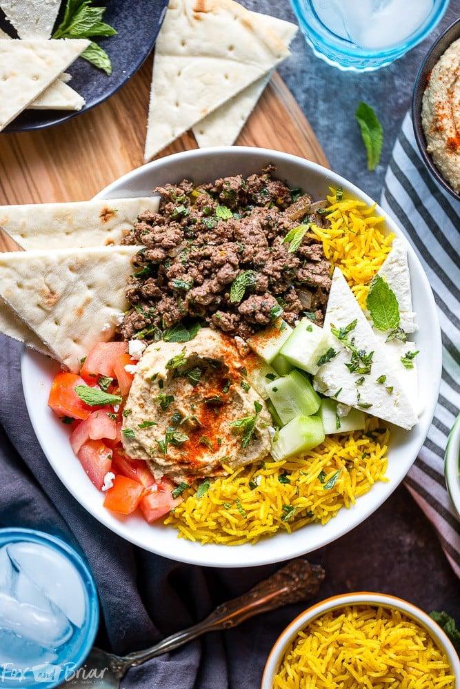 Raw ground lamb being mixed with Greek herbs and spices in a bowl