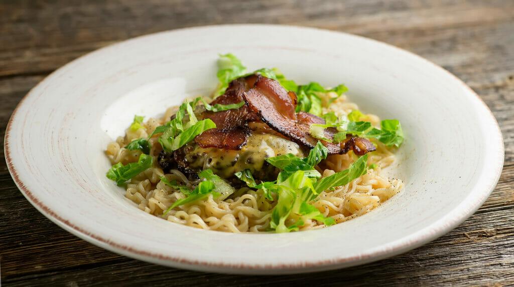 A styled overhead shot of four Pork Ramen Burgers, garnished with fresh green onions and sesame seeds, on a rustic wooden board.