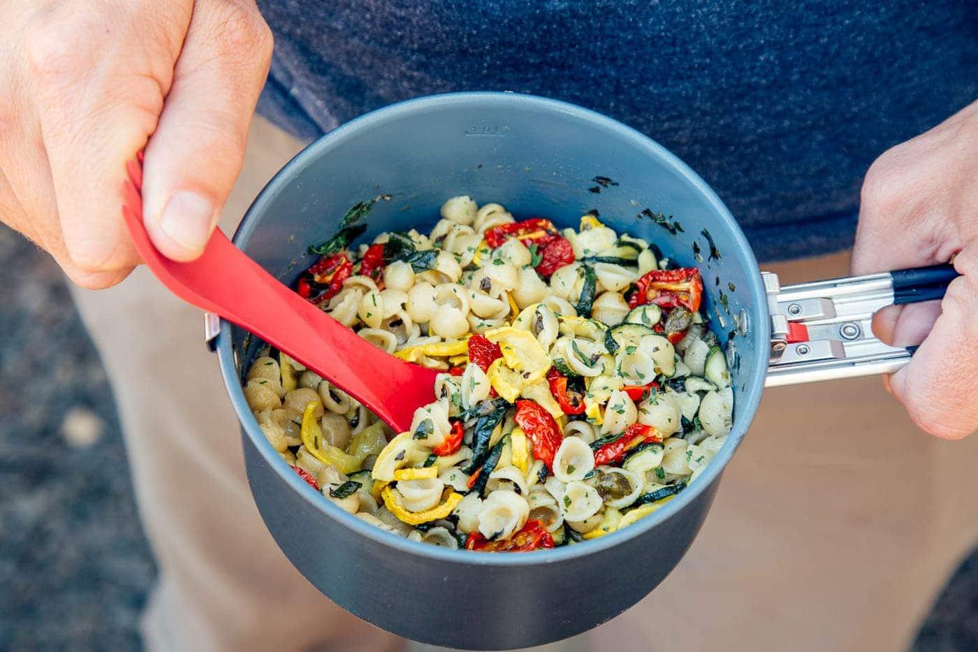 A person enjoying a pasta primavera dish outdoors.