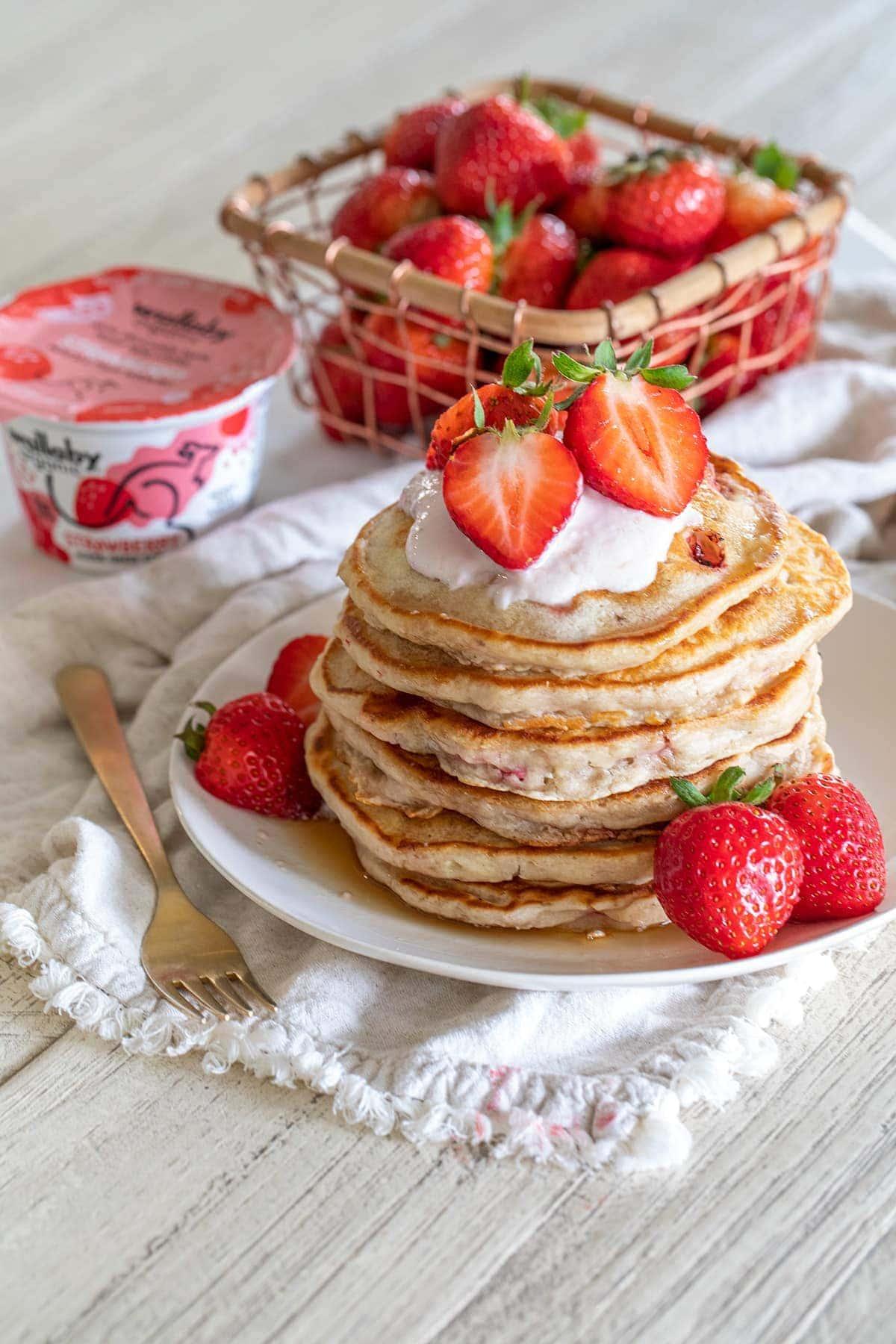 A stack of fluffy strawberry pancakes topped with yogurt and fresh strawberries