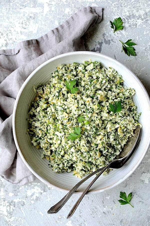 A vibrant bowl of artichoke tabbouleh, garnished with fresh herbs and lemon wedges
