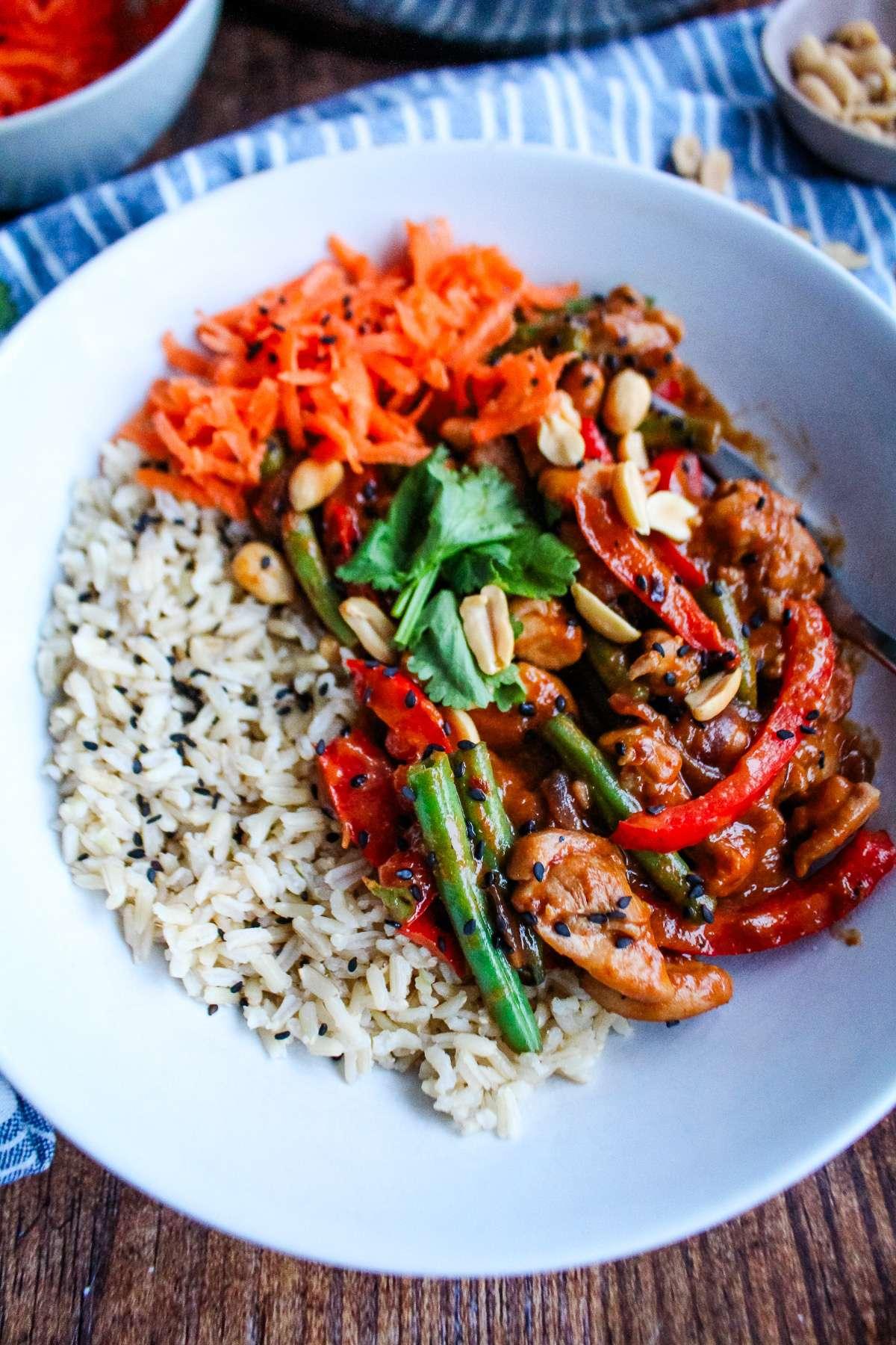 close-up of peanut butter chicken stir-fry served over rice with garnish