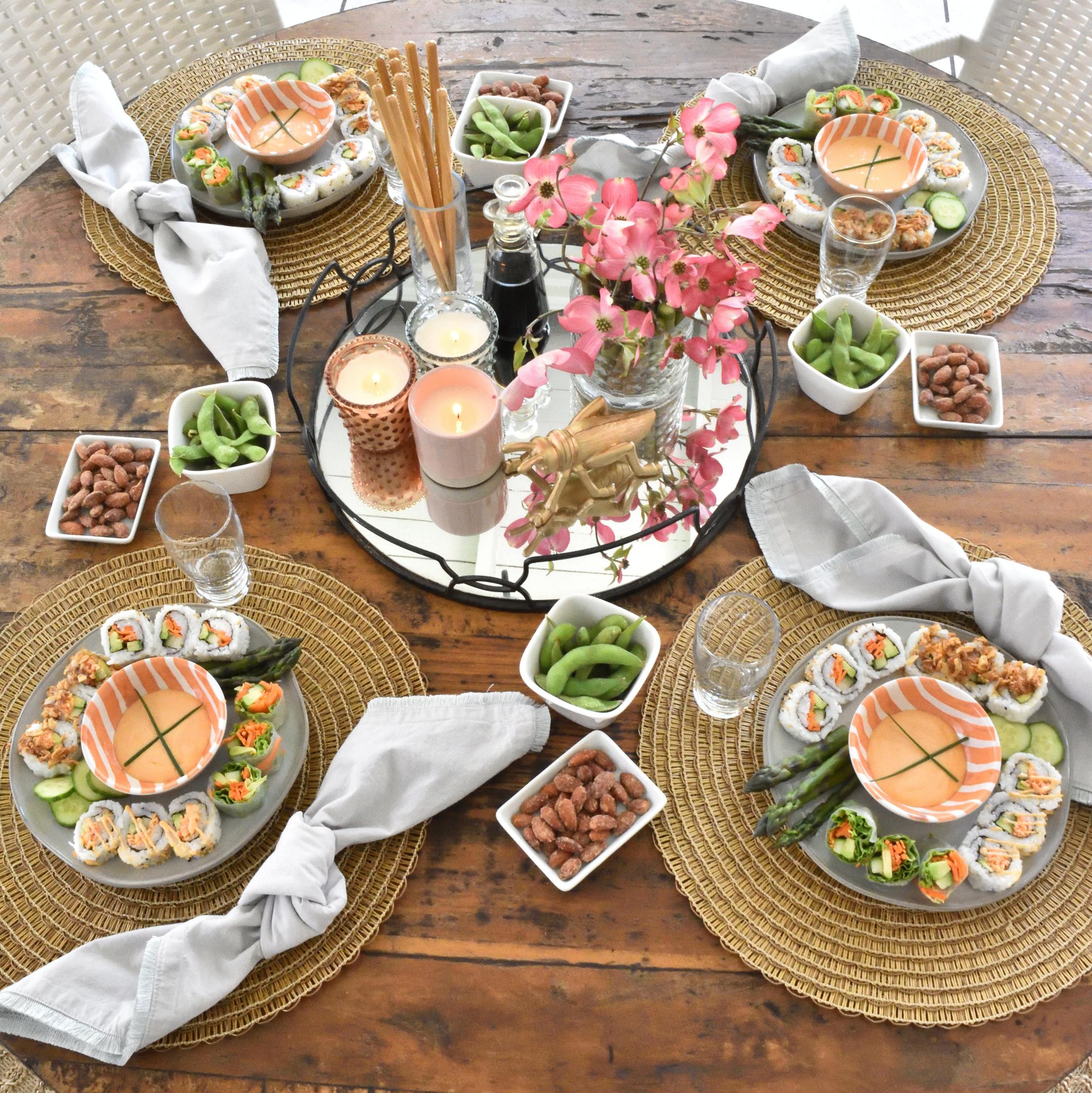A table set for an outdoor party, with a platter of edamame and shrimp spring rolls in the center.