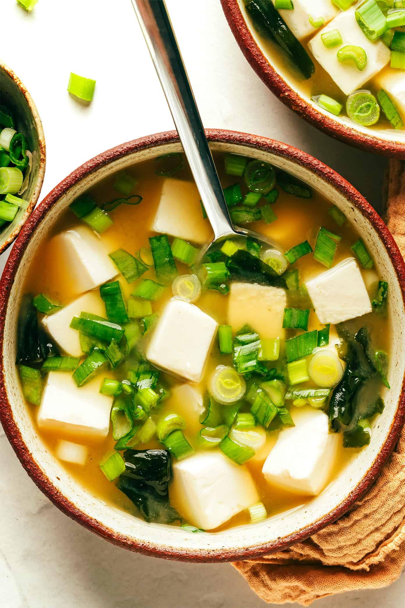 A steaming bowl of miso soup with tofu and seaweed, garnished with scallions