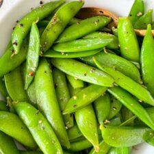 close up shot of person squeezing lemon over cooked eggs and sugar snap peas