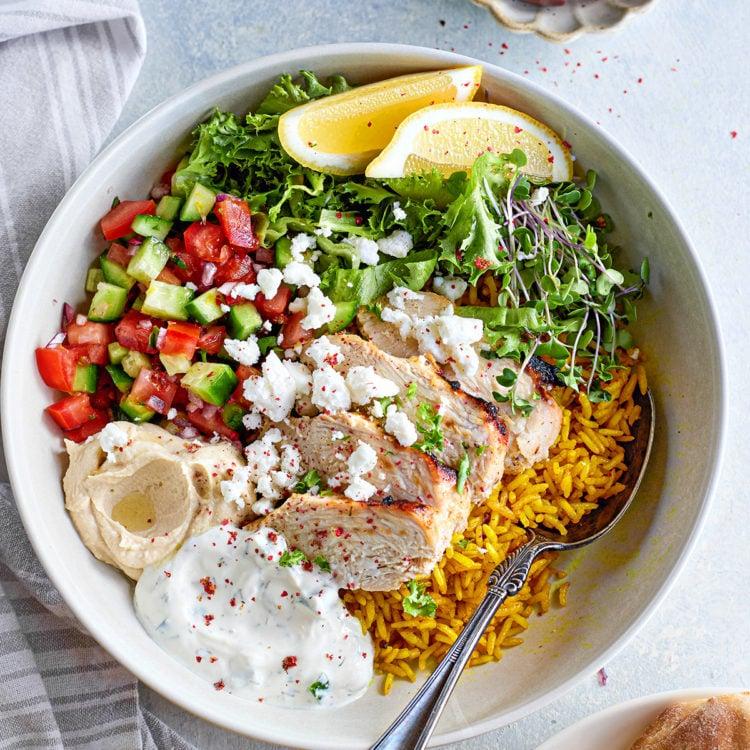Vibrant Greek chicken bowl with tzatziki, feta, and fresh vegetables on a rustic wooden table, bright natural light