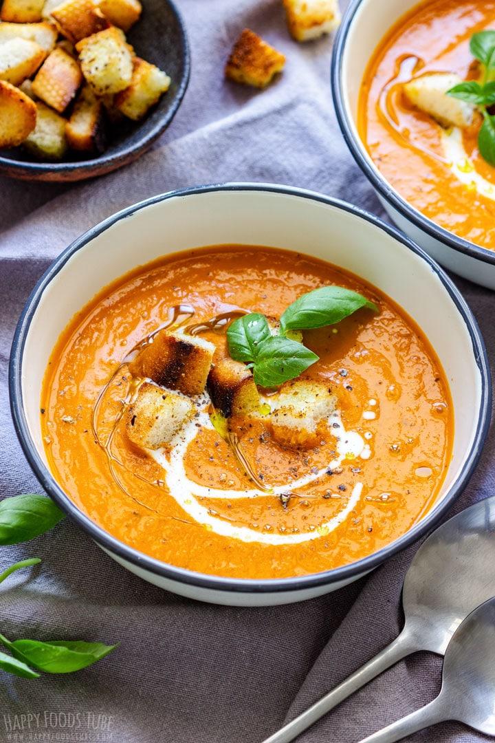 Close-up shot of a bowl of creamy tomato soup stew garnished with fresh basil and a swirl of cream.