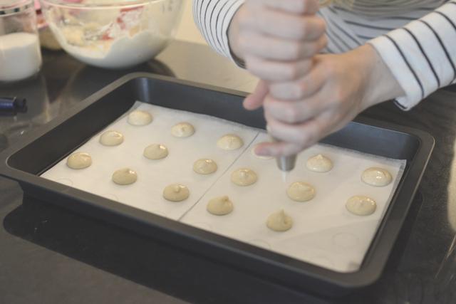 A close up of the macaron batter being piped onto a baking sheet