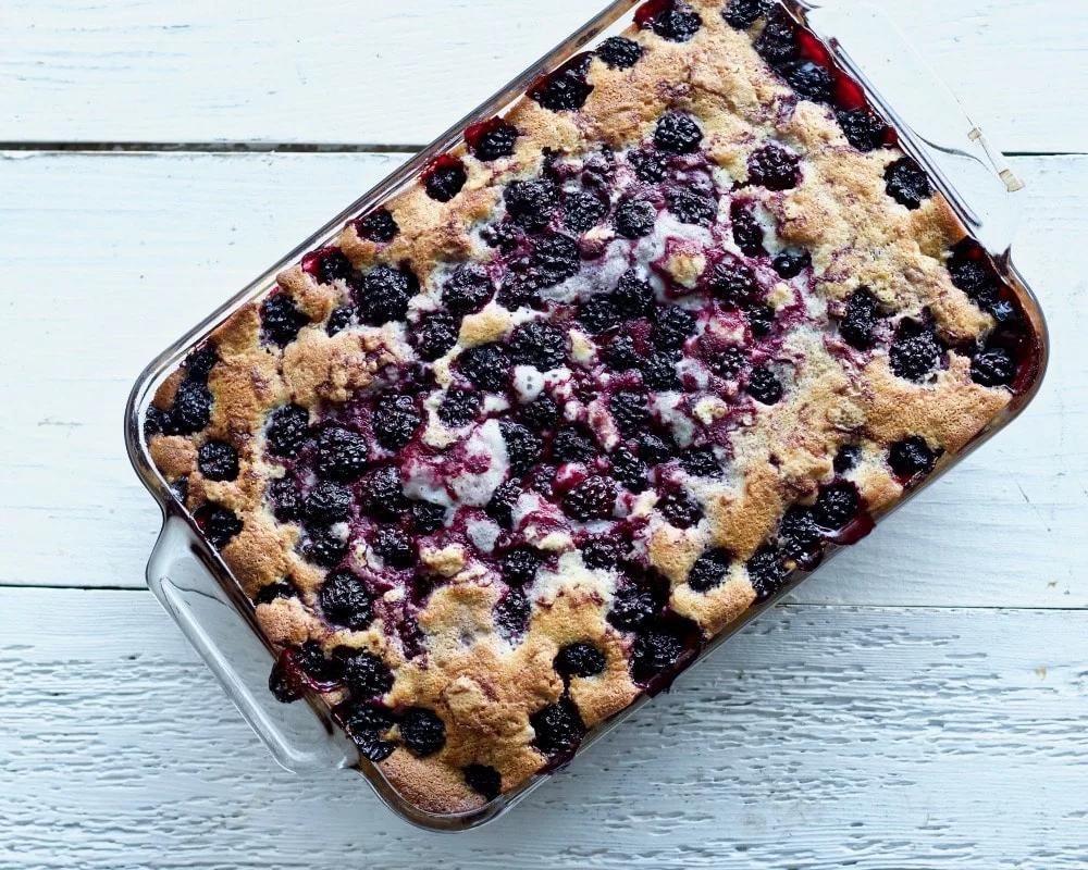 A rustic 9x13 inch baking dish filled with a golden-brown blackberry cobbler topped with a generous dollop of creamy cashew cheese