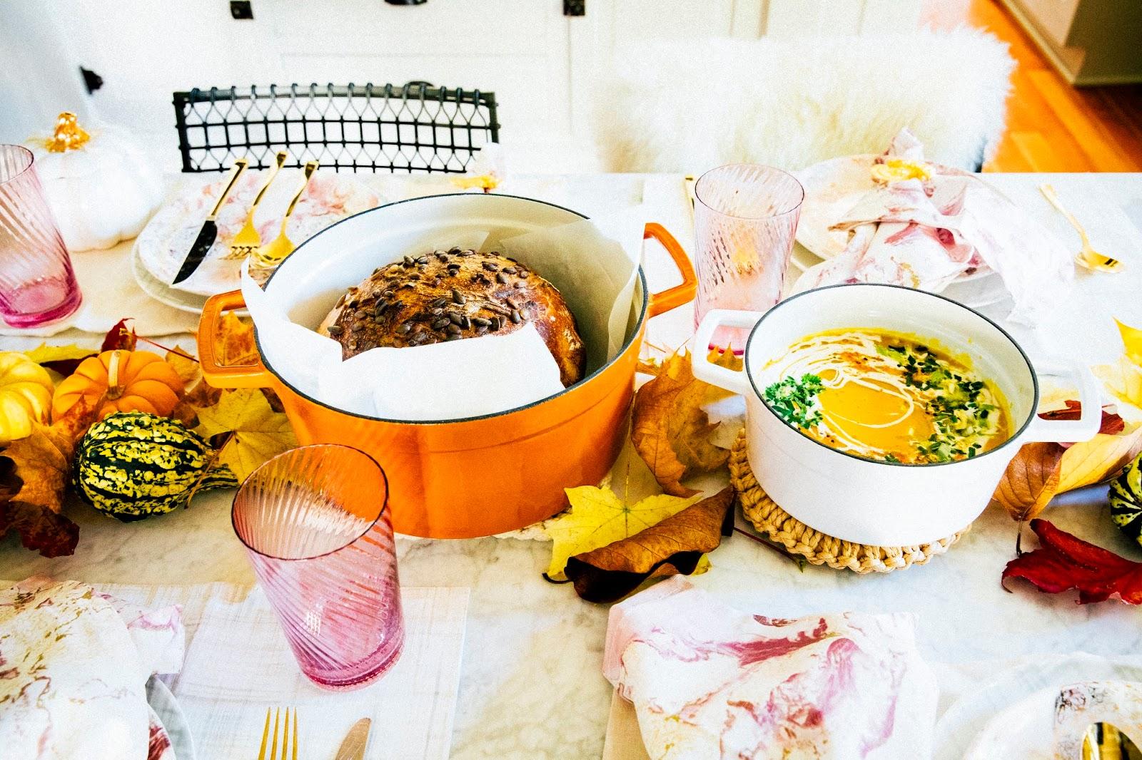 A table set for a fall-themed dinner party, featuring a large bowl of pumpkin soup in the center.