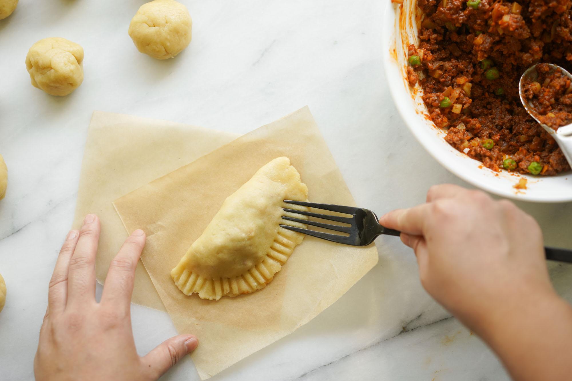 A person's hands carefully crimping the edges of an empanada