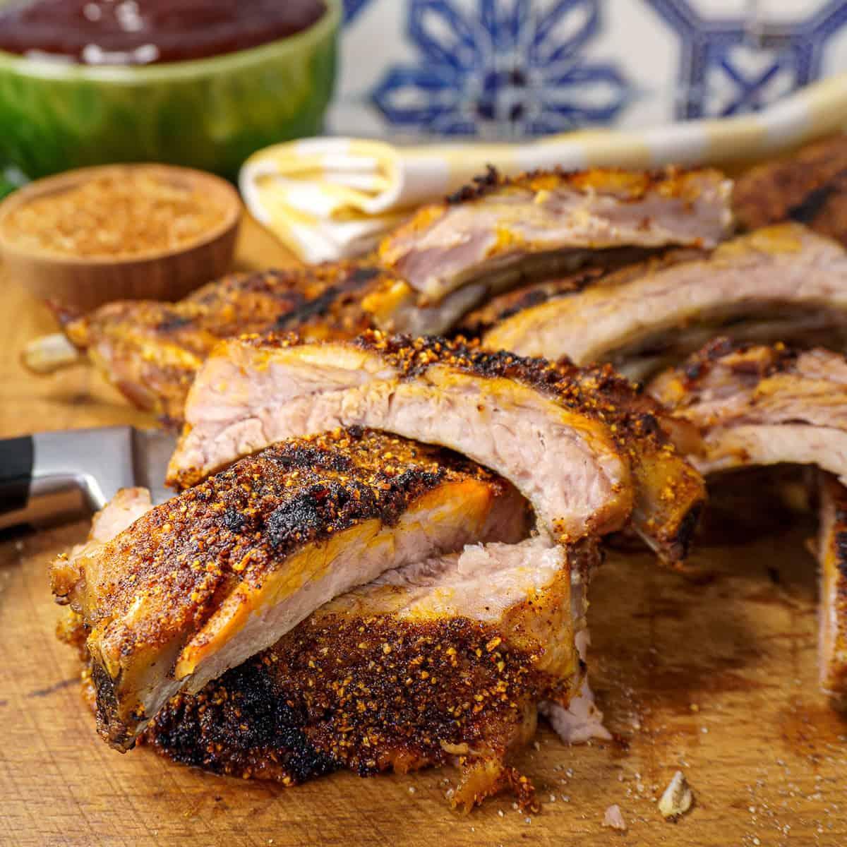 Smoked ribs on a wooden cutting board, with onion rub in a bowl in the background